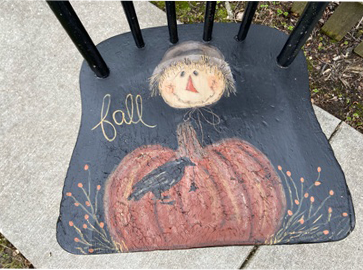 closeup of seat on the black wooden chair with pumpkin and scarecrow painted on seat