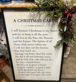 White wooden sign decorated with greens with a Christmas Carol poem on it.