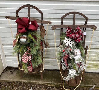 two antique wooden sleds decorated with greenery, bows and seasonal decorations