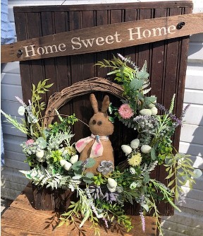 Wooden wall hanging with wreath, flowers and bunny on it.